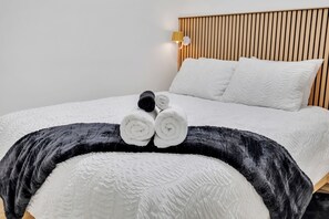 A neatly made bed with a white duvet and a black throw blanket, accompanied by rolled towels. - Stylish Suite by Airport/Fast Wi-Fi/Free Driveway Parking/Sleeps 4/Self Check-in (Calgary)