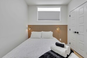 Une chambre à coucher avec un lit, une fenêtre, une armoire et une table de chevet avec une lampe.