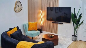 Ein modernes Wohnzimmer mit einem bogenförmigen schwarzen Sofa, einem hellblauen Sessel und einer Holzwand.