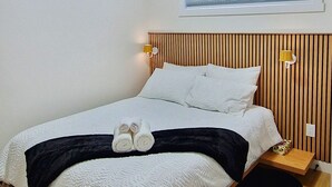 Ein modernes Schlafzimmer mit einem großen Bett, einem Fenster mit Jalousien, einer Deckenleuchte und einem hölzernen Kopfteil.