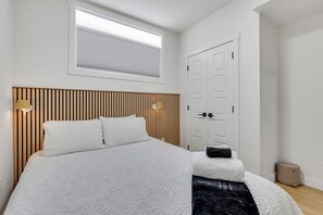 Ein Schlafzimmer mit einem Bett, einem Fenster mit Jalousien, einer Tür und einem Nachttisch mit Lampe.