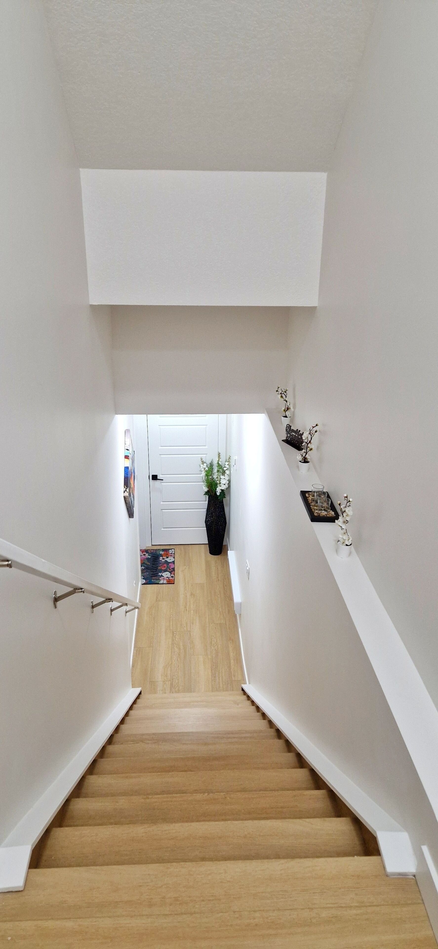 A staircase with a wooden finish, white walls, and a door at the top.