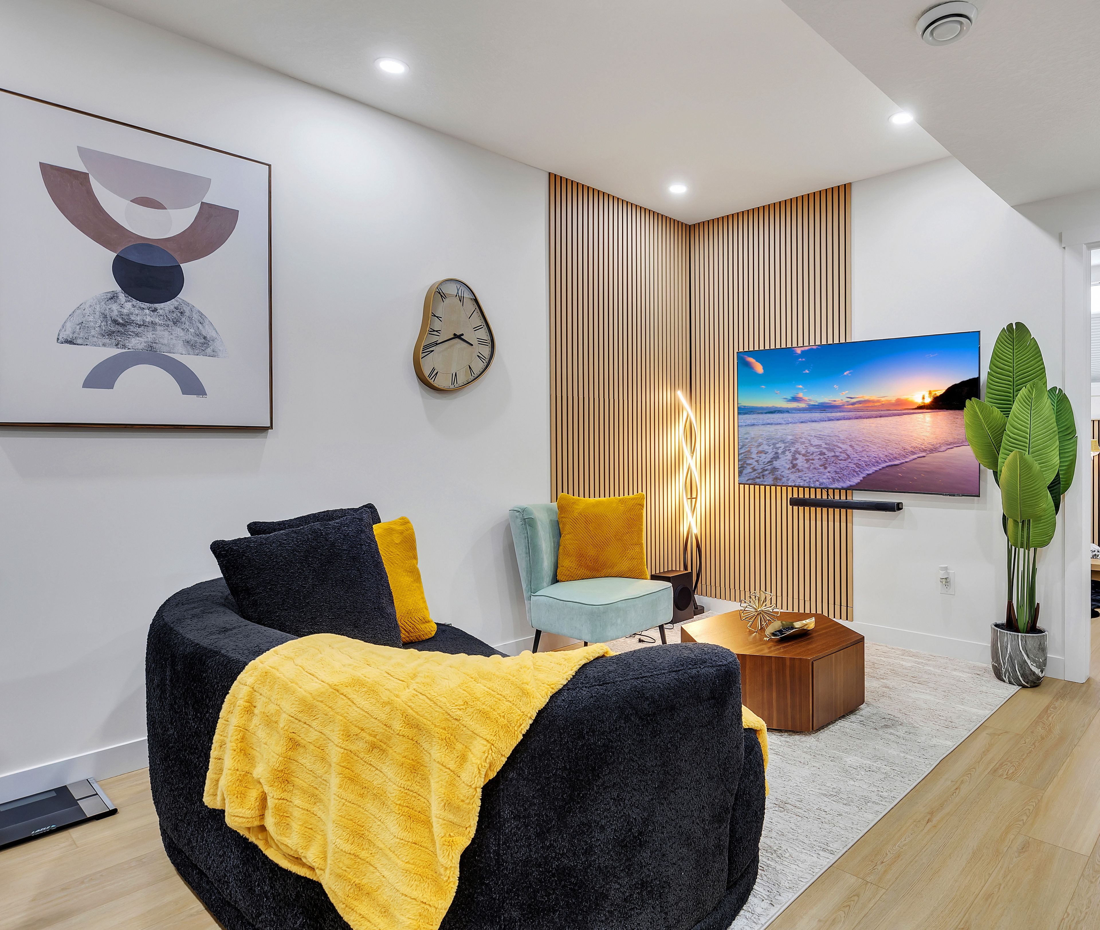 A modern living room with a flat-screen TV, a clock, and a large plant.