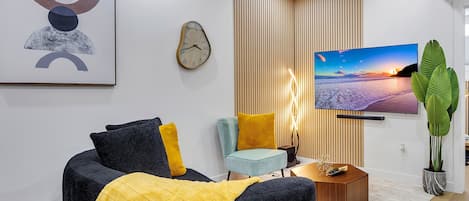 A modern living room with a flat-screen TV, a clock, and a large plant.