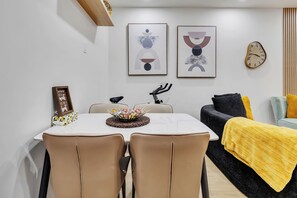 Ein modernes Wohnzimmer mit Essbereich, ausgestattet mit Tisch und Stühlen, einer Couch, einer Uhr und abstrakter Kunst an der Wand.