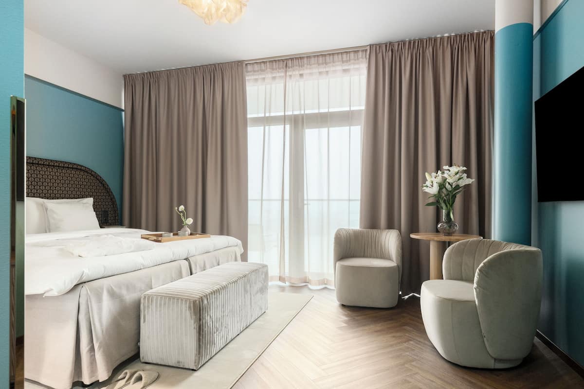 A hotel room with a bed, two chairs, a small table, and a TV.