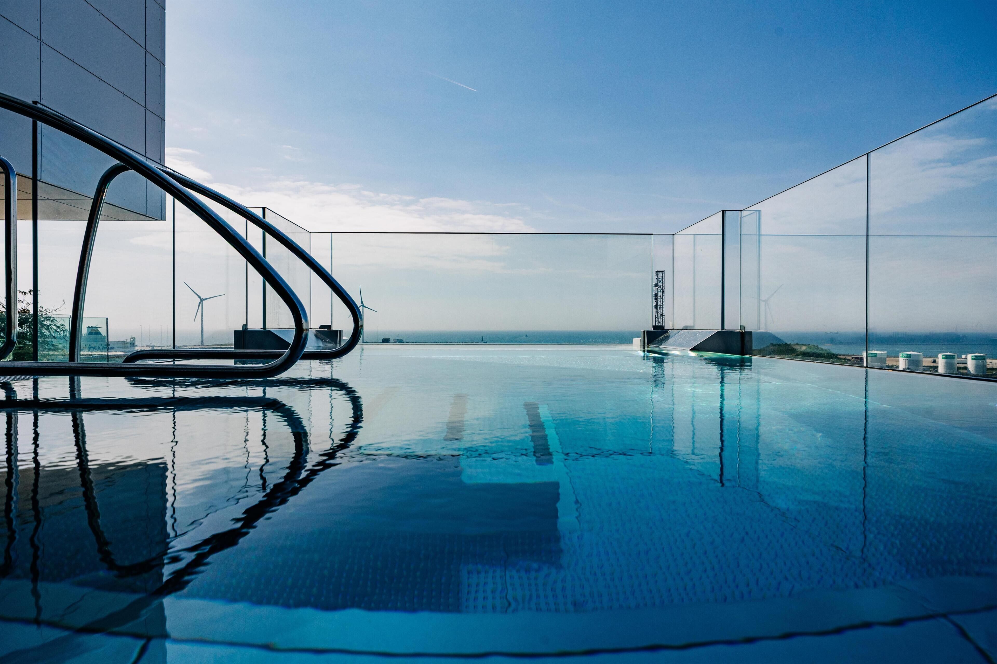 Una piscina infinita moderna con vistas despejadas al océano y aerogeneradores a lo lejos.