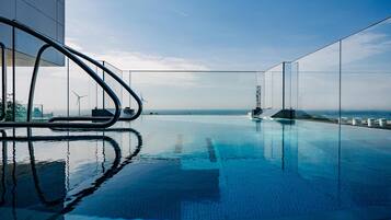 Una piscina infinita moderna con vistas despejadas al océano y aerogeneradores a lo lejos.