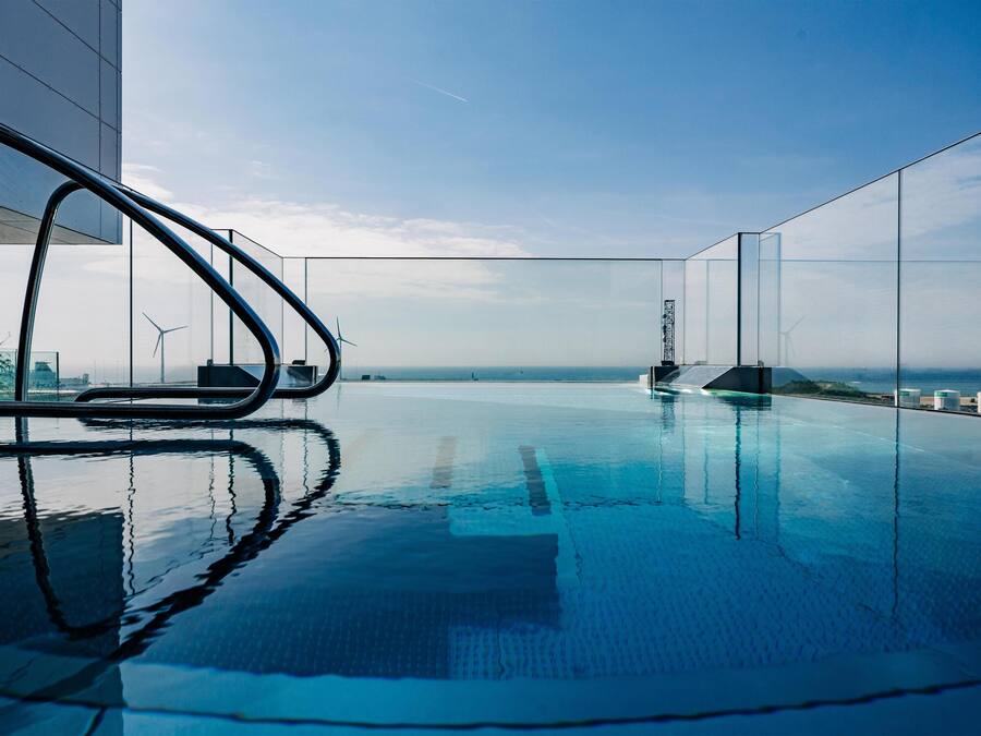 Una piscina infinita moderna con vistas despejadas al océano y aerogeneradores a lo lejos.