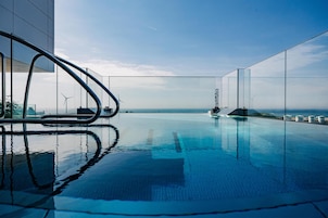 Una piscina infinita moderna con vistas despejadas al océano y aerogeneradores a lo lejos.