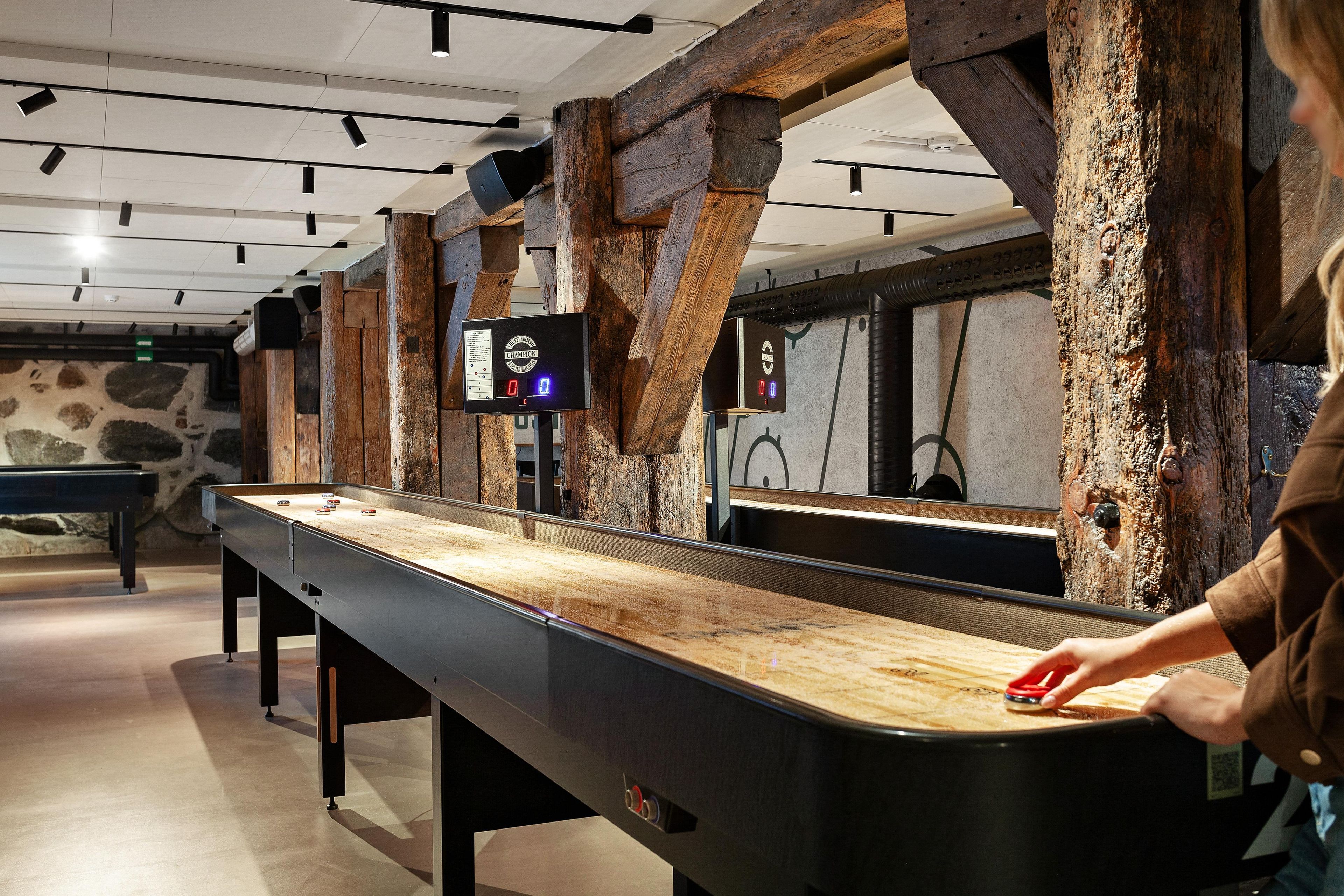 Una mesa de billar con un marcador digital en una sala con vigas de madera a la vista y paredes de piedra.