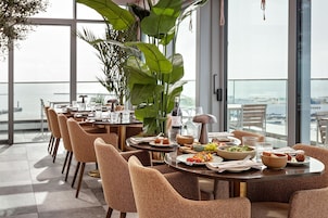 Comedor con mesas redondas, sillas de mimbre y vistas a la ciudad.
