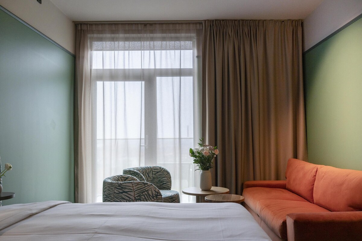 A hotel room with a bed, a sofa, a chair, a small table, and a window with curtains.