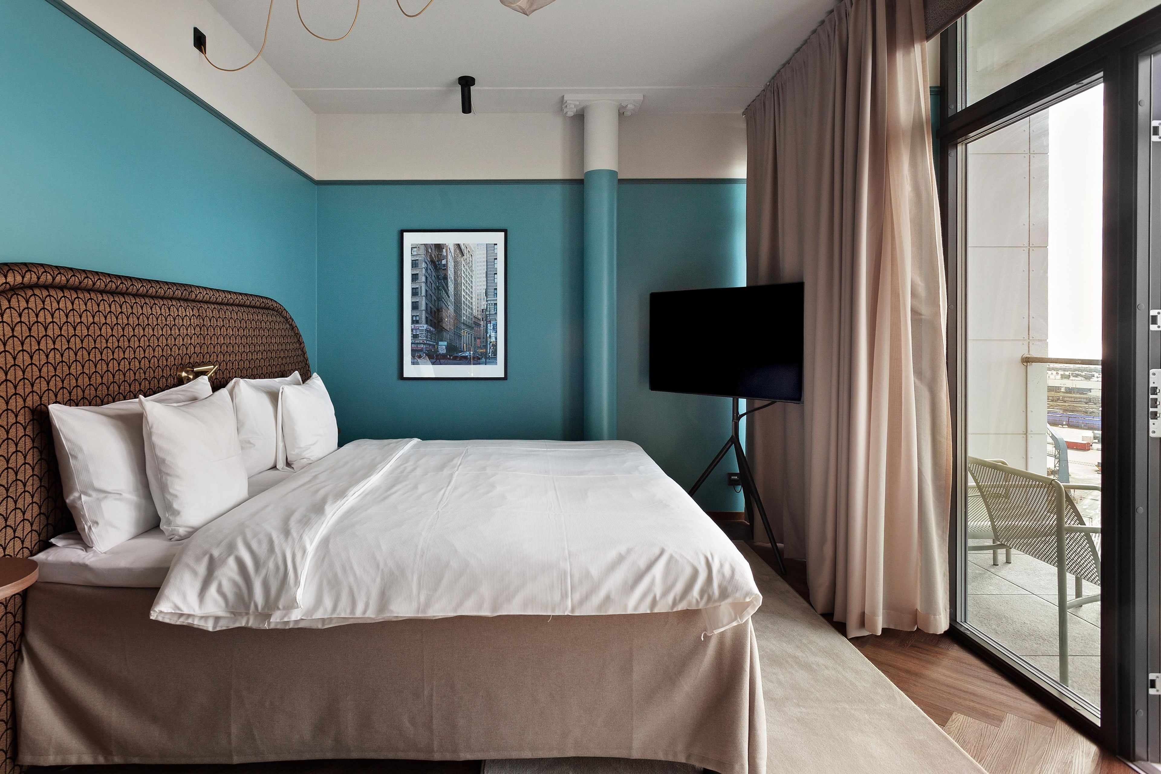 A hotel room with a large bed, a flat-screen TV, a framed picture on the wall, and a view through the window.