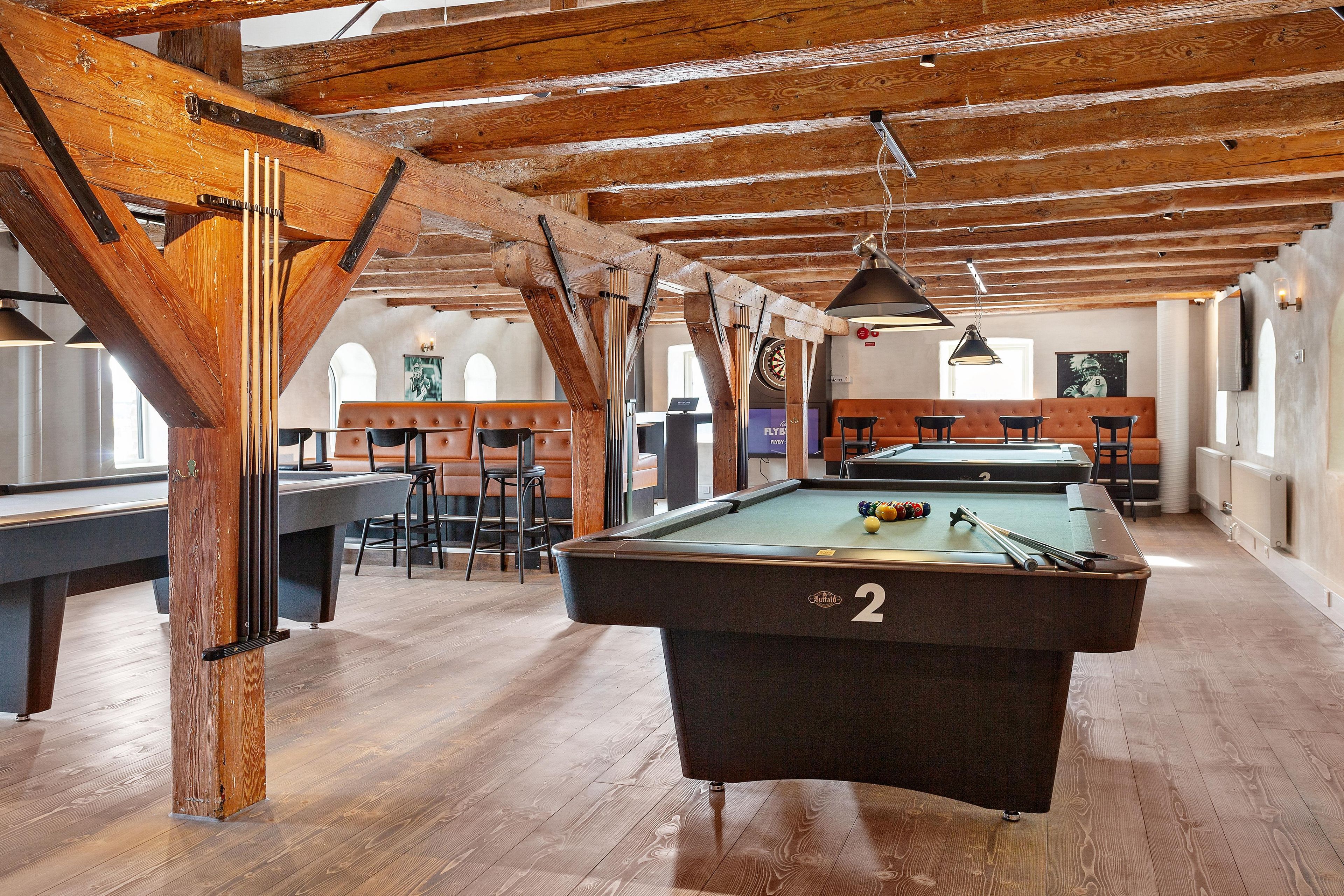 A pool table in a room with wooden beams, a dartboard, and a billiards table.