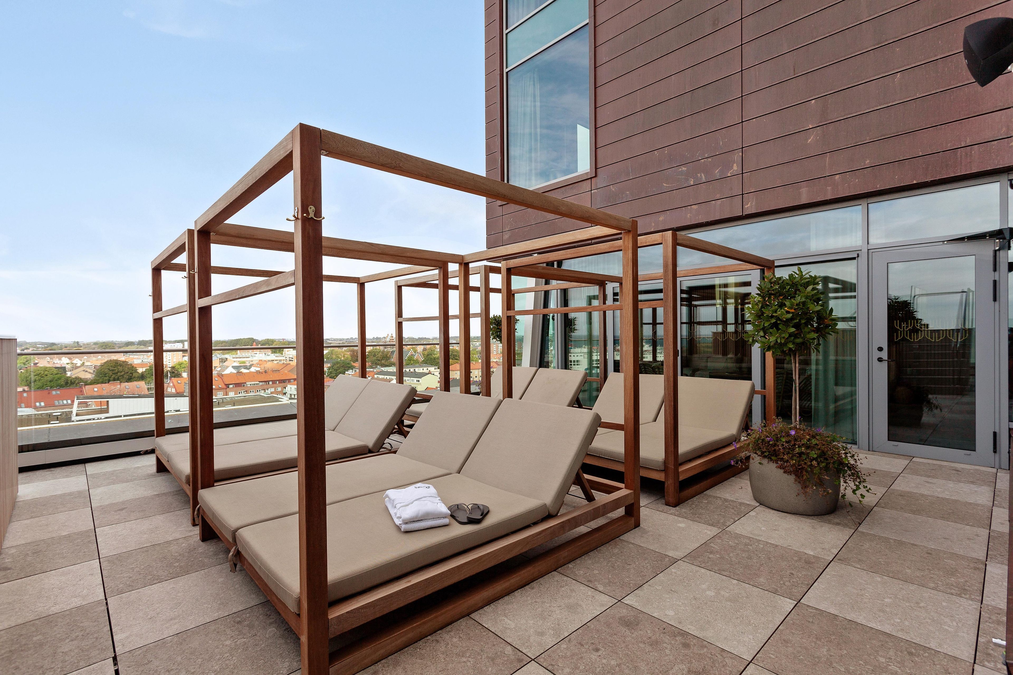 Une terrasse sur le toit, avec des chaises longues en bois, un pot de fleurs et une vue sur le paysage urbain.