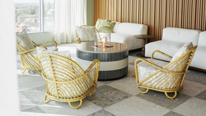 A modern living room with wicker furniture, a round coffee table, and a view of the city through large windows. - Willow, Worldhotels Crafted (Trelleborg)