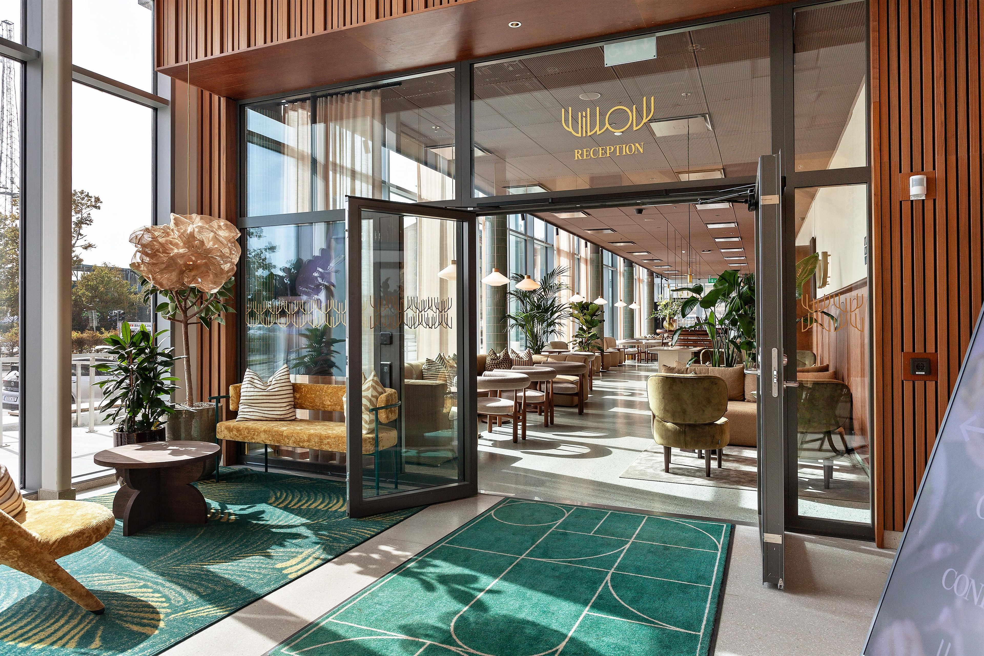 En hotellobby med modern design, med en receptionsdisk, en sittgrupp och stora fönster som släpper in naturligt ljus.