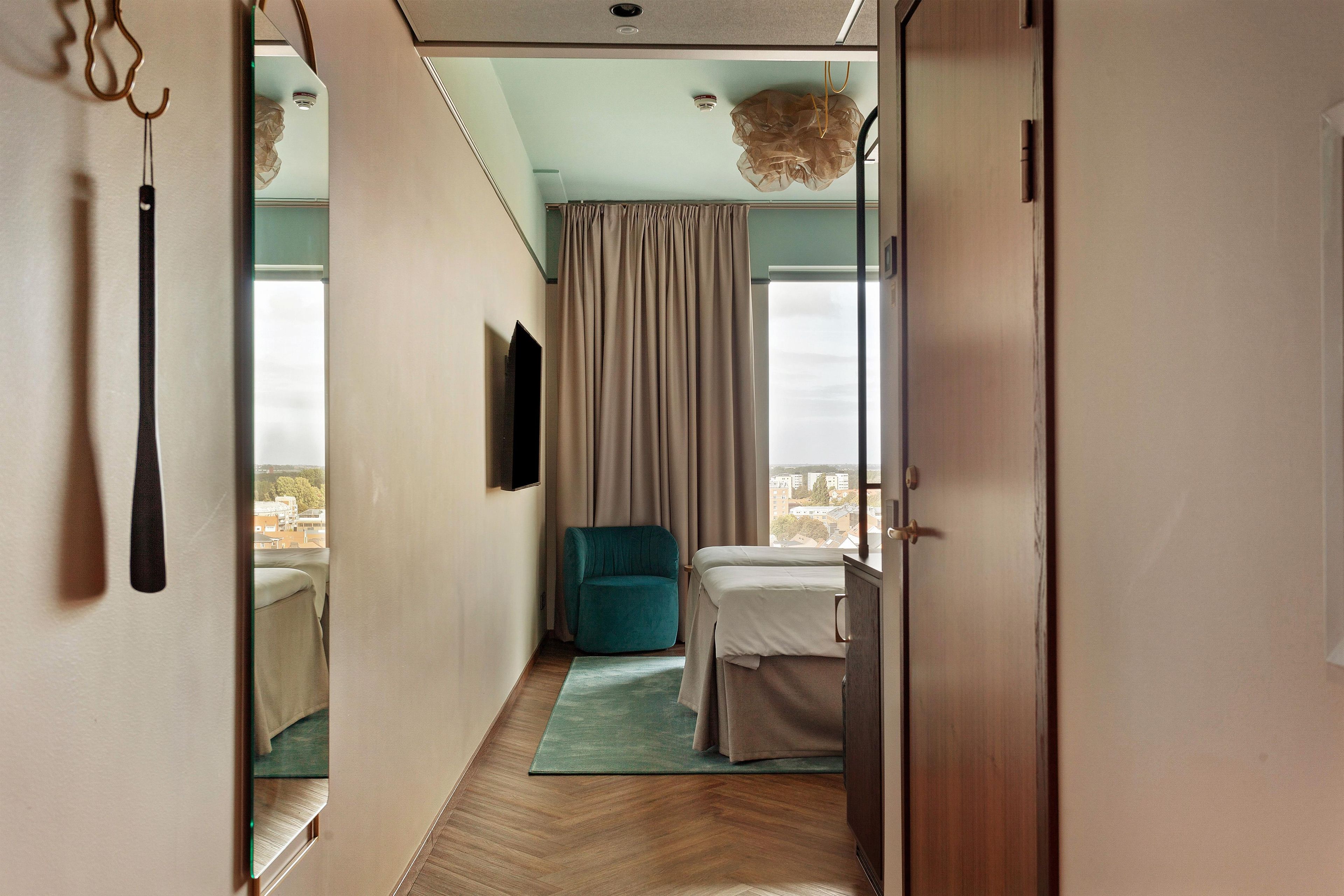 A hotel room with a bed, a chair, a television, and a view of the city.