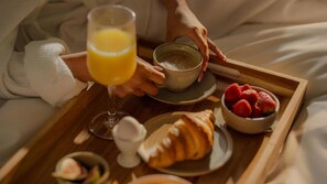 A breakfast tray with a croissant, strawberries, a glass of orange juice, and a cup of coffee on a bed.