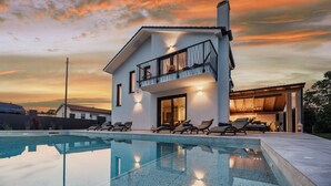 A modern house with a swimming pool, a balcony with a railing, and a well-lit interior. - Villa Enja in tranquille village with heated salted pool (Vintijan)