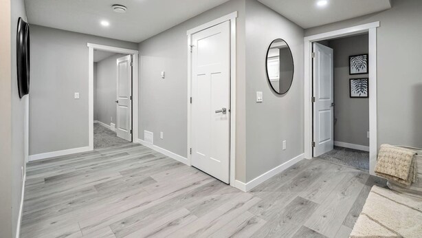 Un pasillo con paredes grises, puertas blancas y piso de madera gris.