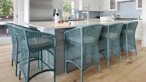 A modern kitchen with white cabinets, a large island, and teal wicker chairs. - Private Pool | Great for Families | Tides of Joy (Isle of Palms)