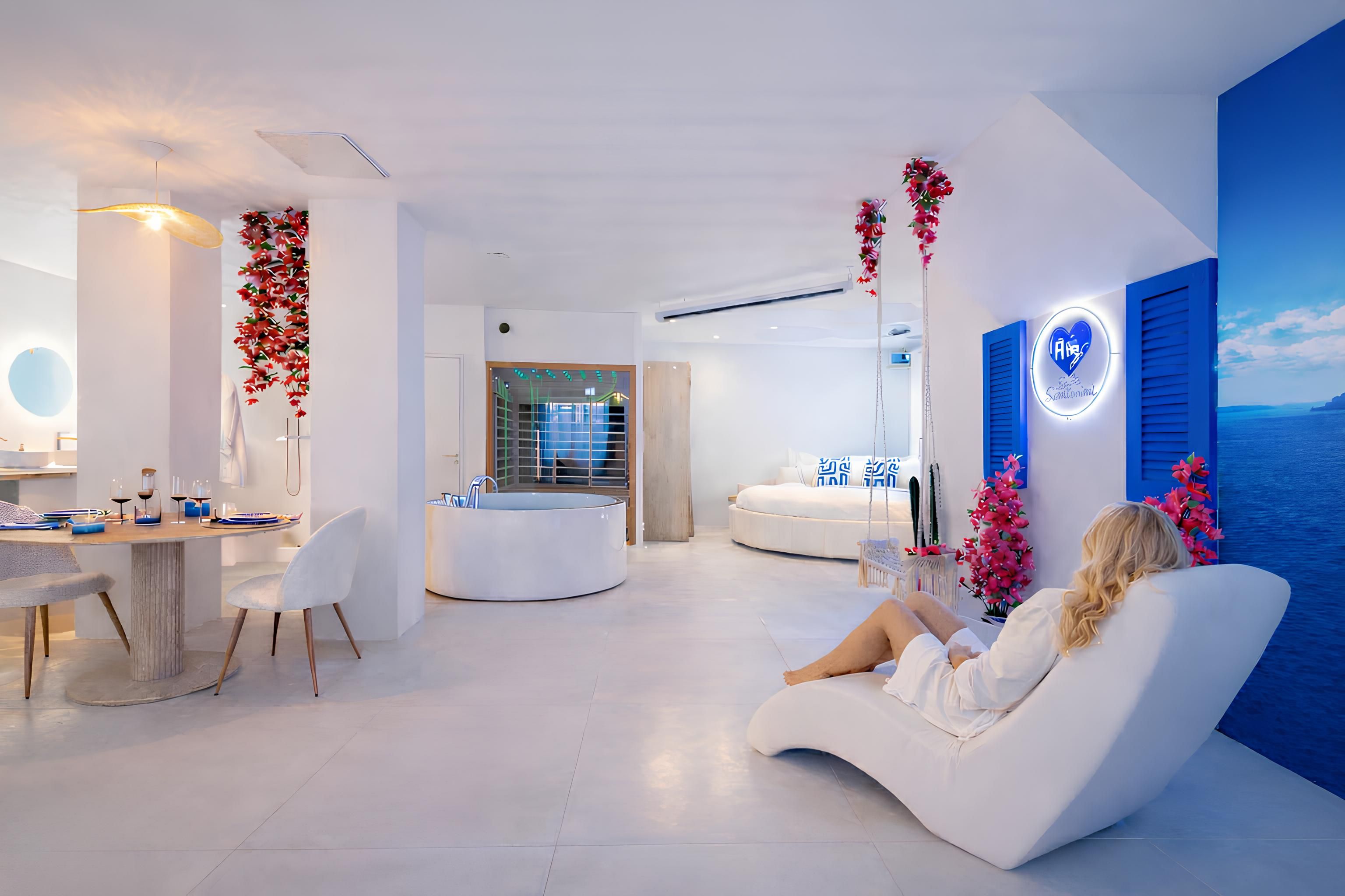 Una sala de estar moderna con un sofá blanco, un comedor con una mesa redonda y vista al mar a través de un ventanal.
