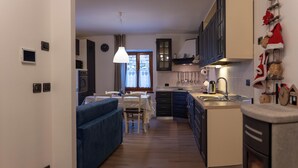 A modern kitchen with dark cabinets, a dining area with a blue sofa, and holiday decorations. - Casa Del Torchio: Apartment with vineyard view in Trentino (Valternigo)