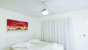Une chambre à coucher avec un lit, un ventilateur de plafond, un tableau et une fenêtre avec des rideaux.
