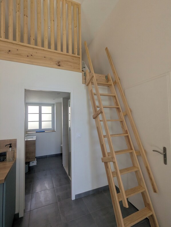 Une pièce avec une mezzanine en bois, une échelle en bois, une fenêtre, un évier et une porte.