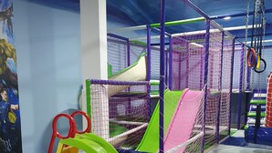 Un espace de jeux intérieur avec un toboggan, un filet d’escalade et une piscine à balles.