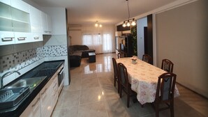Une cuisine moderne avec des meubles blancs, un plan de travail noir et un coin repas agrémenté d’une nappe à motifs floraux.