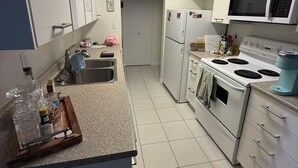 A kitchen with white cabinets, a microwave, a stove, and a refrigerator. - 2 bedroom condo available for FIFA (Burnaby)