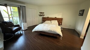 A bedroom with a wooden bed, a dark leather sofa, and a large window with curtains. - 2 bedroom condo available for FIFA (Burnaby)