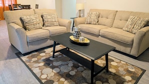 Un salon avec deux canapés beige, des coussins à motifs, une table basse noire et un tapis à motifs.