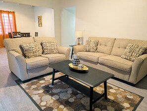 A living room with two beige sofas, patterned cushions, a black coffee table, and a patterned rug. - Suite Little Coconut: Cozy modern 1BR/1BA house in Antigua with AC (Saint George)