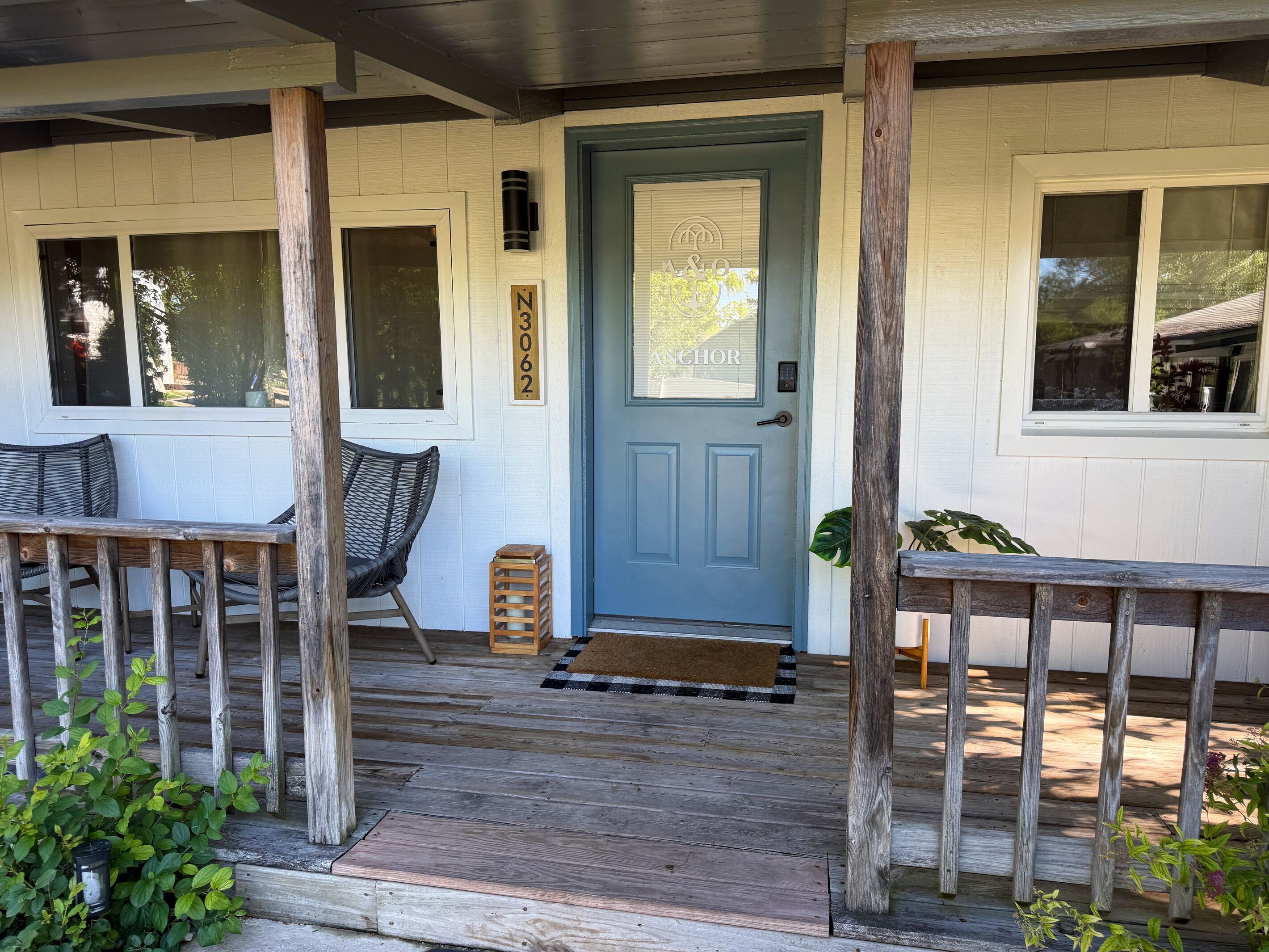 A porch with wooden railings, a blue door, and a small wooden stool.