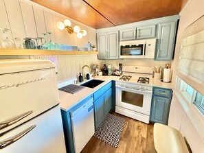 A compact kitchen with a white refrigerator, a microwave, a stove, and blue cabinets. - Tide Cabin | Walk to Lake Como + Fire Pit + Grill (Lake Geneva)
