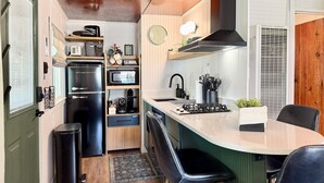 Una cucina compatta con frigorifero, microonde e piano cottura. Sono presenti due sedie nere e un piccolo cestino.