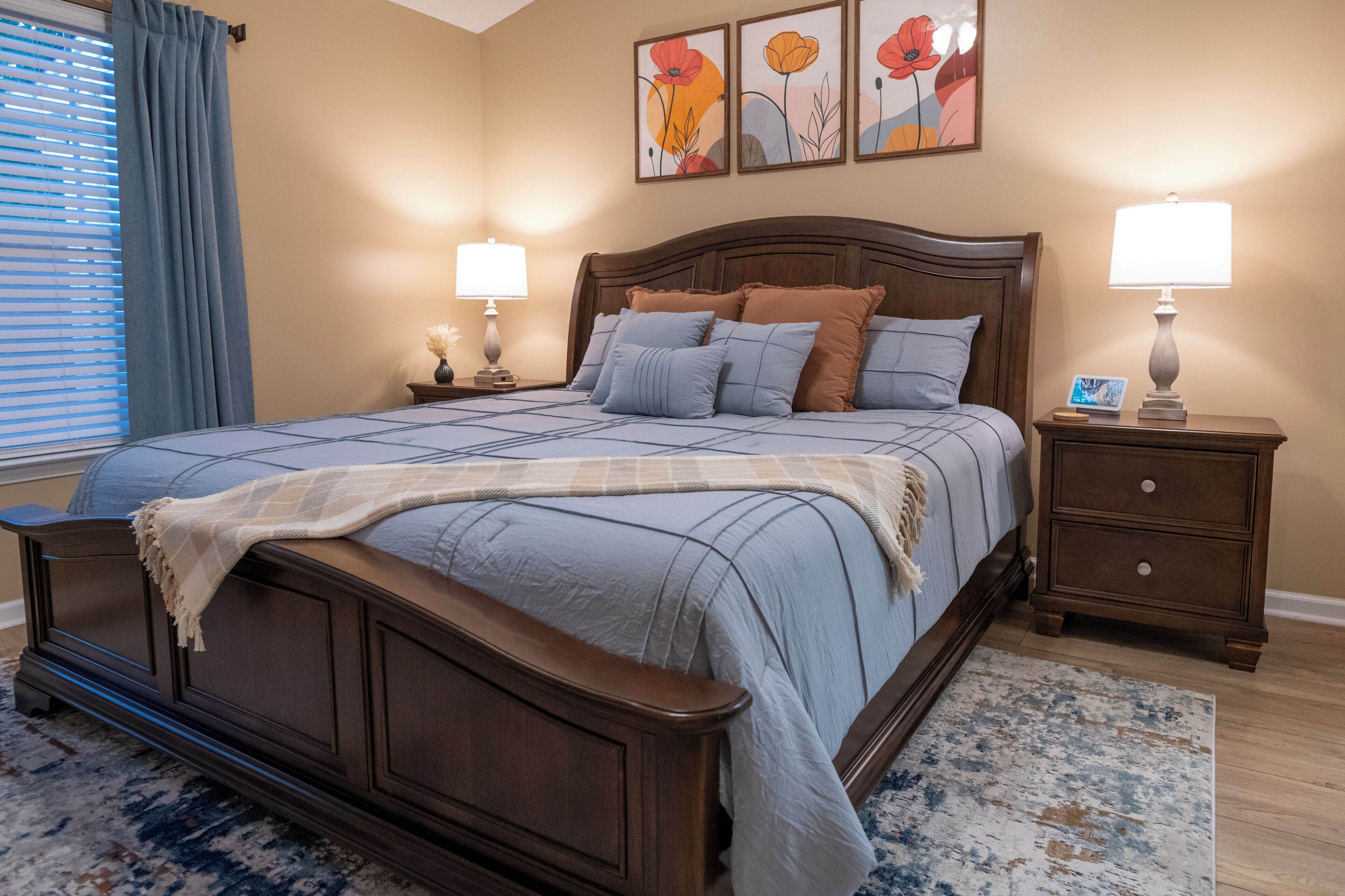 Une chambre à coucher avec un grand lit, deux tables de chevet, une commode, une lampe et un cadre photo posé sur la commode.