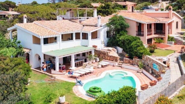 A villa with a swimming pool, outdoor seating, and a lush garden. - Seafront villa (Cala Caterina)