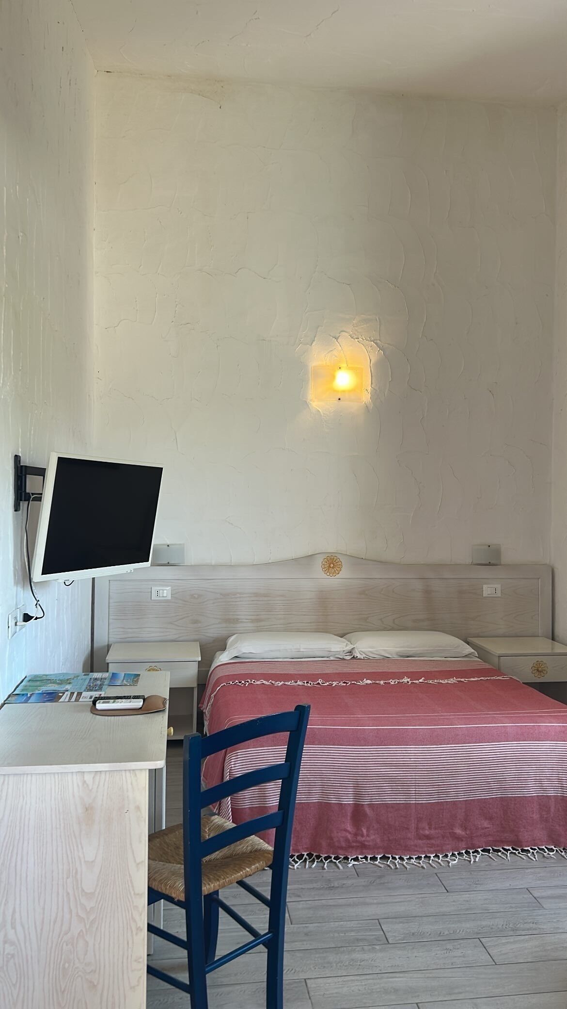 Un dormitorio con cama, escritorio, silla, lámpara de pared y reloj de pared.