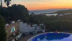 A swimming pool with a sunset view, stone walls, and potted plants. - Seafront villa (Cala Caterina)