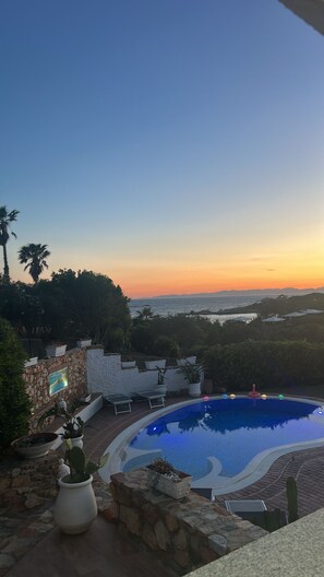 A pool with a sunset view, stone walls, and potted plants. - Seafront villa (Cala Caterina)