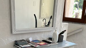 A white console table with drawers, a mirror above, and a window with a view of greenery. - Seafront villa (Cala Caterina)