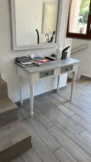 A white console table with drawers, a mirror above, and a window with a view of greenery. - Seafront villa (Cala Caterina)