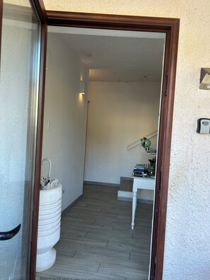 A hallway with a white wall, a wooden floor, a white pedestal with an umbrella, and a small table with a lamp.