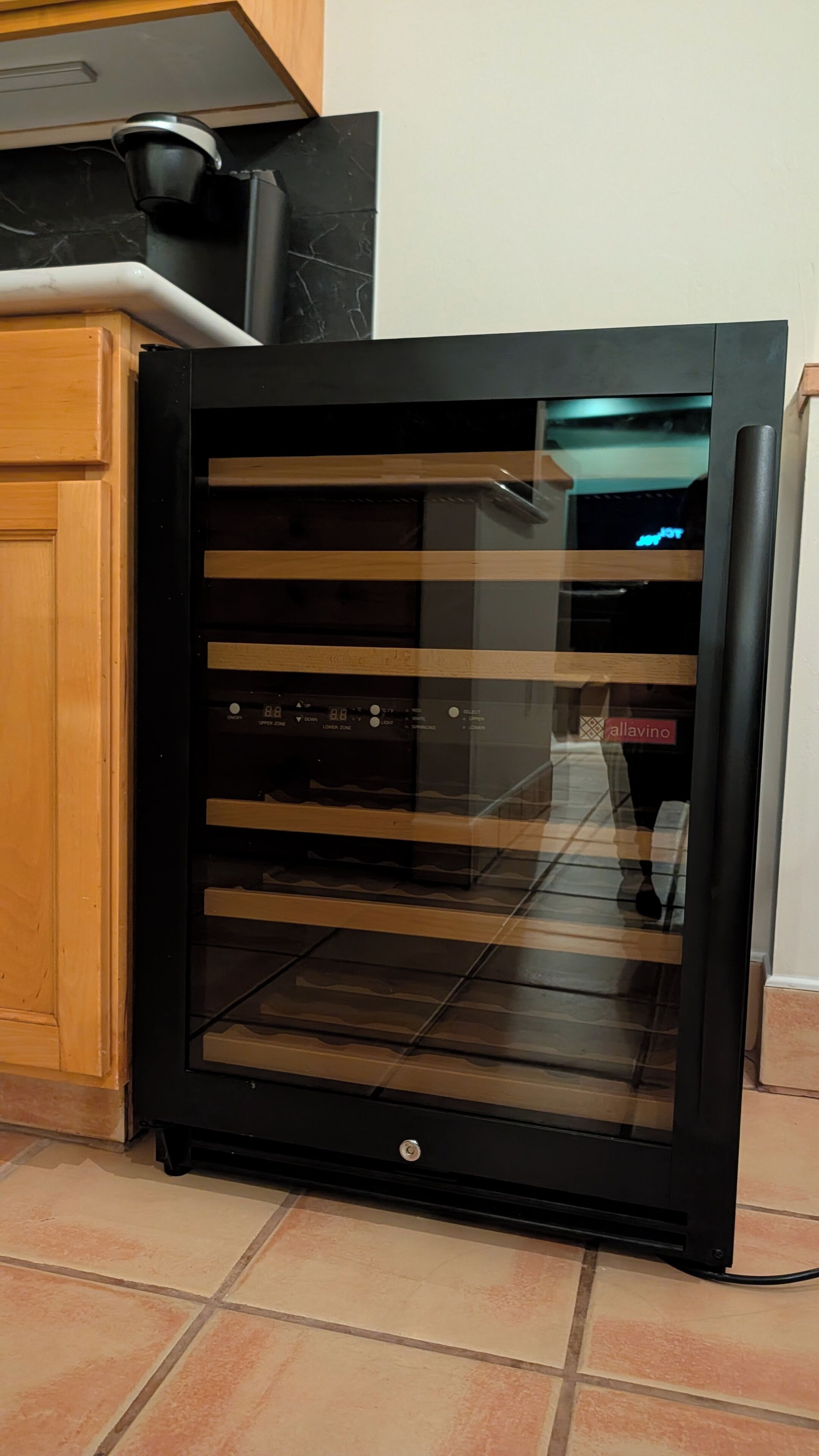 Un refrigerador negro con puerta de vidrio, un panel de control con botones y el nombre de marca 'allavino' en la puerta.