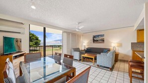 A spacious living area with a glass dining table, comfortable seating, a flat-screen TV, and a balcony with a scenic view. - Relax & Explore: Spacious 2BR Suite at Maui Schooner Resort (Kihei)